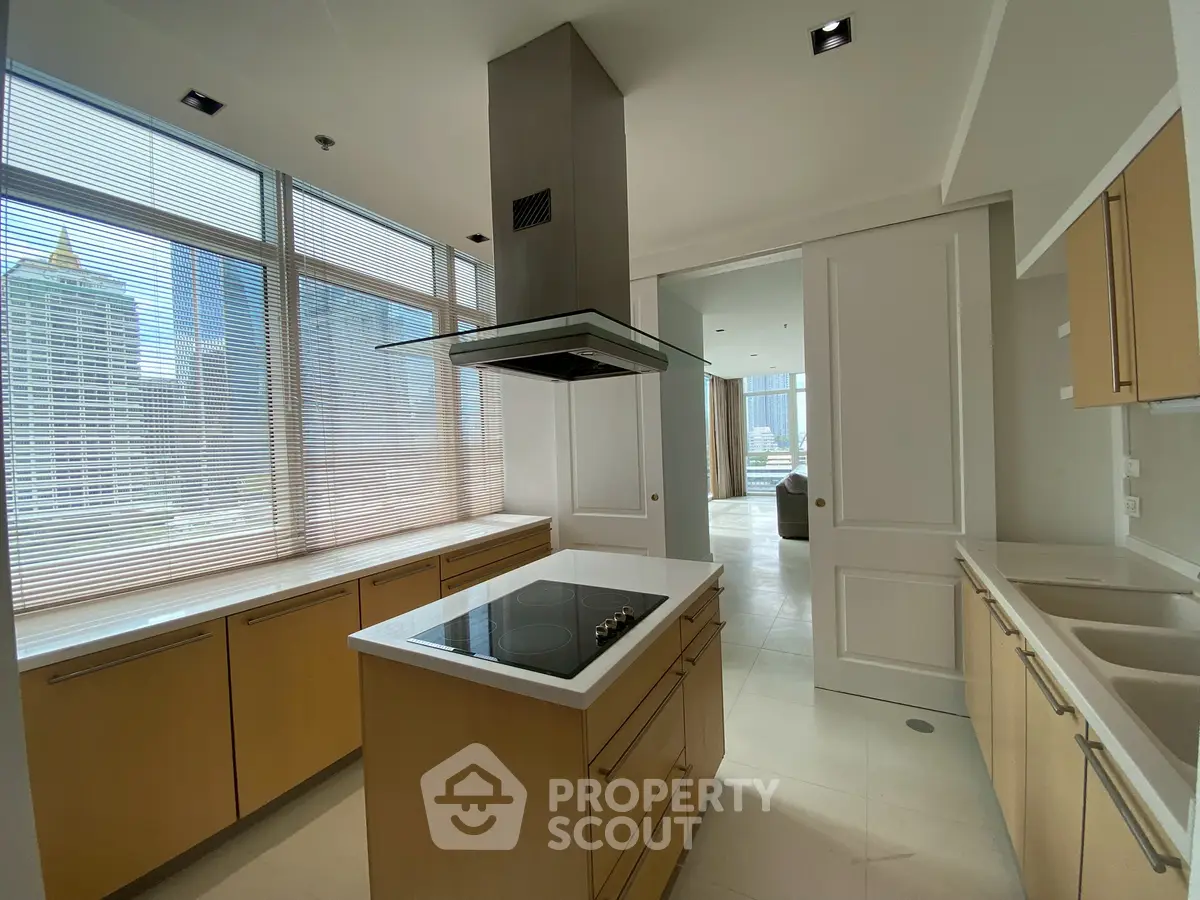 Modern kitchen with sleek design and city view, featuring an island with induction cooktop and ample natural light.