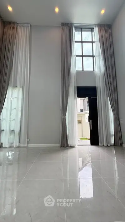 Spacious modern living room with high ceilings and large windows, offering abundant natural light and elegant curtains.