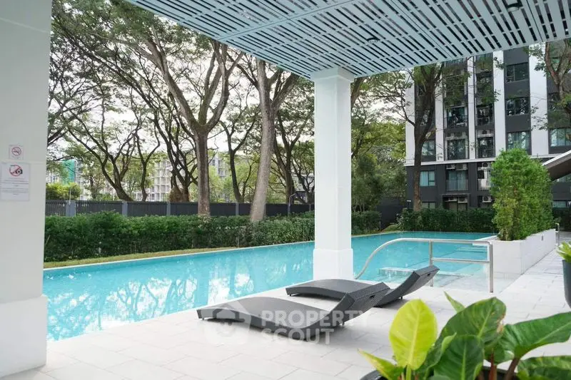 Luxurious outdoor pool area with modern lounge chairs and lush greenery in a high-end residential complex.