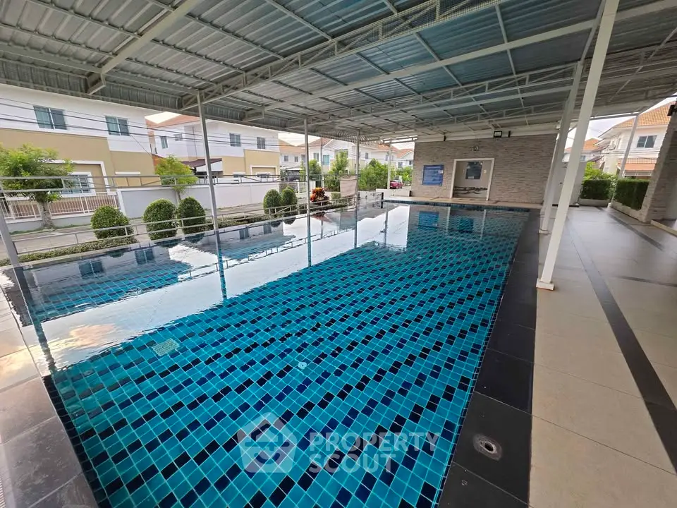 Spacious covered swimming pool in modern residential complex with tiled flooring and landscaped surroundings.