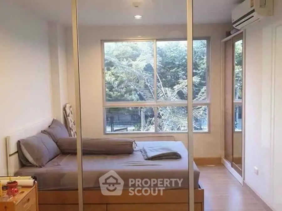 Modern bedroom with large window and mirrored wardrobe, offering a serene view of lush greenery.