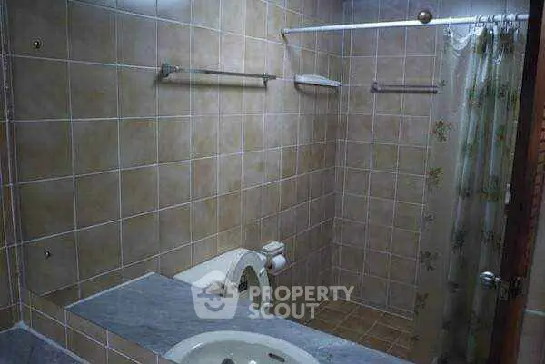 Cozy bathroom with tiled walls and shower curtain, featuring a sink and toilet.