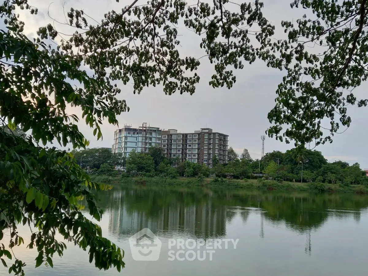 Scenic view of modern apartment building by a tranquil lake surrounded by lush greenery.