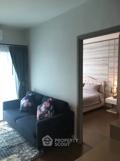 Cozy living room with dark sofa and floral pillows, adjacent to a stylish bedroom with elegant decor.