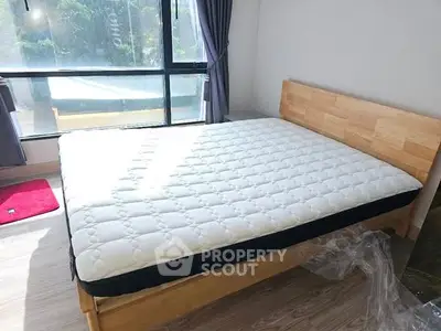 Bright bedroom with large window and wooden bed frame, perfect for relaxation.