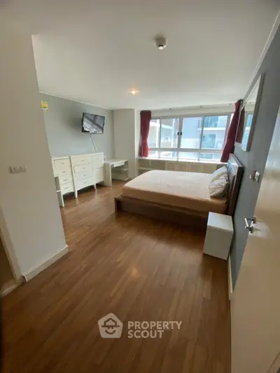 Spacious bedroom with wooden flooring and large window in modern apartment