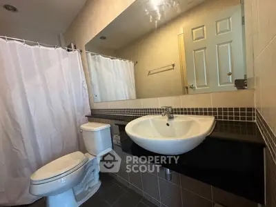 Modern bathroom with sleek sink and large mirror, featuring a tiled shower area.
