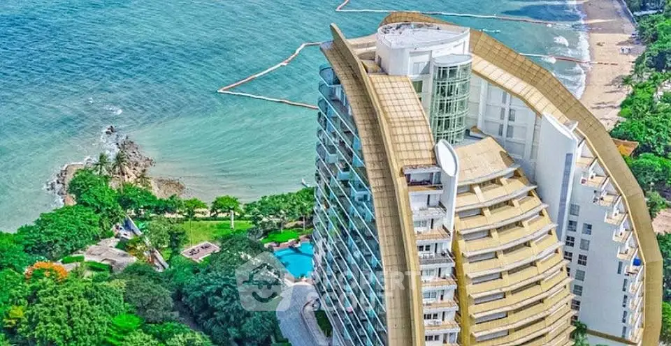 Stunning aerial view of luxury beachfront condominium with lush greenery and ocean backdrop.