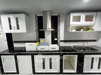 Modern kitchen with sleek black countertops and white cabinetry, featuring a stainless steel range hood.