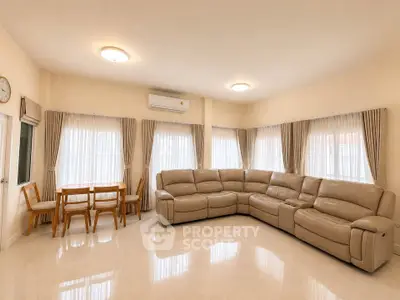 Spacious living room with elegant corner sofa and dining area, featuring large windows and natural light.