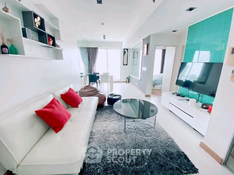 Modern living room with stylish decor, white sofa, and large TV in a bright apartment.