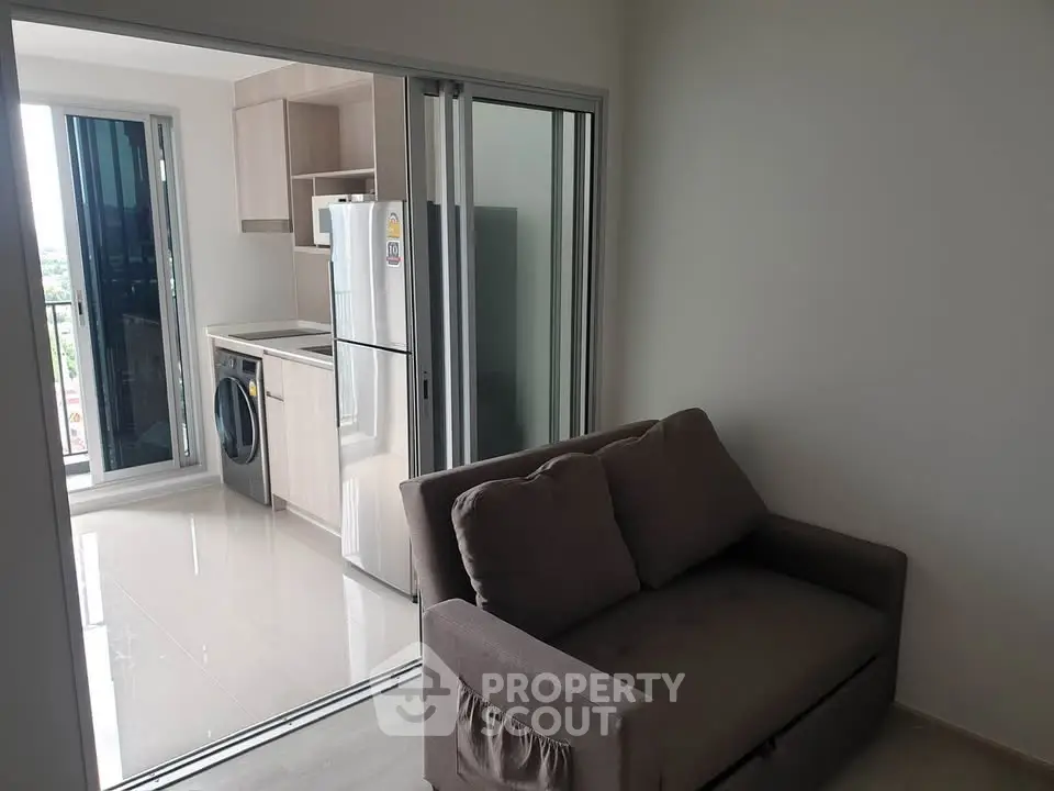 Modern apartment with compact kitchen and cozy living area, featuring a washing machine and fridge.