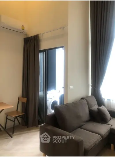 Modern living room with high ceilings, cozy sofa, and adjacent laundry area with washing machine.