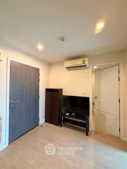 Modern living room with air conditioning and sleek wooden flooring, featuring a TV setup and minimalist decor.