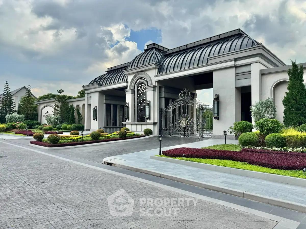 Luxurious estate entrance with elegant architecture and manicured gardens under a cloudy sky.