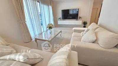 Elegant living room with plush sofas and large TV, featuring natural light and modern decor.