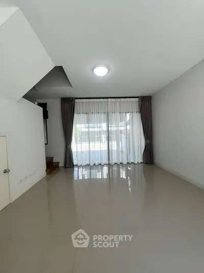 Spacious living room with large window and elegant curtains, perfect for natural light.