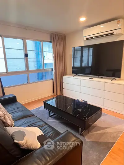 Modern living room with sleek black leather sofa, large TV, and air conditioning, perfect for relaxation.