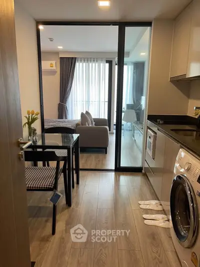 Modern apartment interior with open layout, featuring kitchen and living area with washing machine.