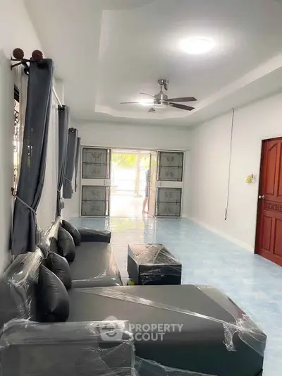 Spacious living room with modern furniture and ceiling fan, featuring large windows for natural light.