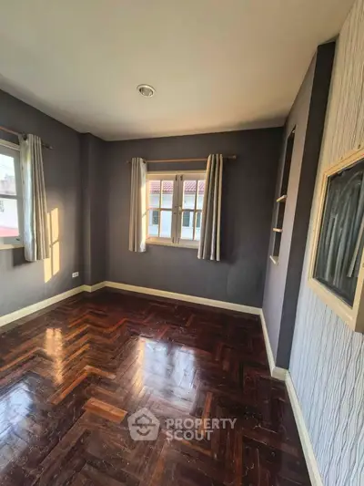 Spacious empty room with elegant parquet flooring and large windows for natural light.