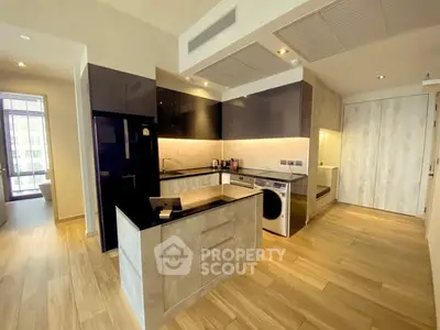 Modern kitchen with sleek black cabinets, integrated appliances, and wood flooring in a stylish apartment.