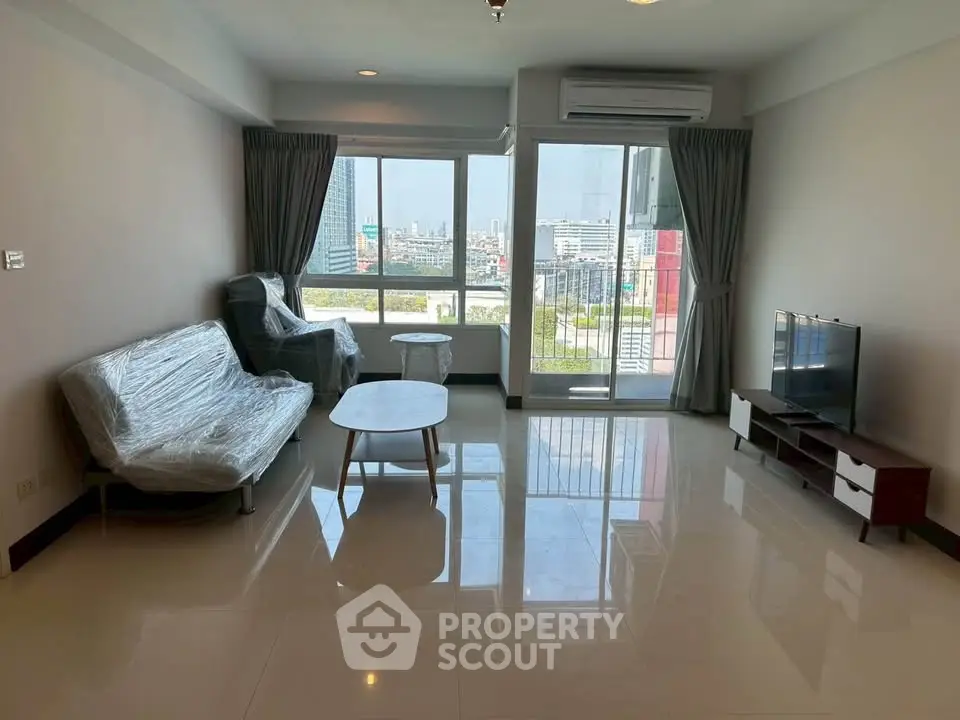 Spacious living room with large windows and city view, featuring modern furniture and natural light.
