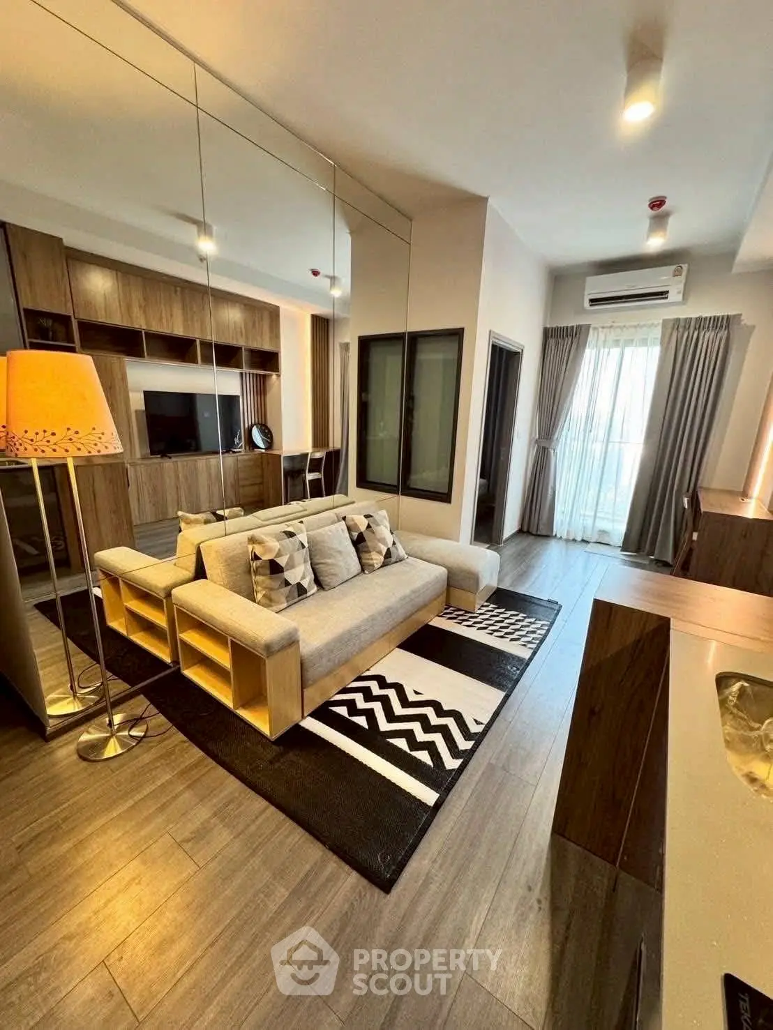 Modern living room with stylish decor and large mirror wall, featuring cozy sofa and elegant lighting.