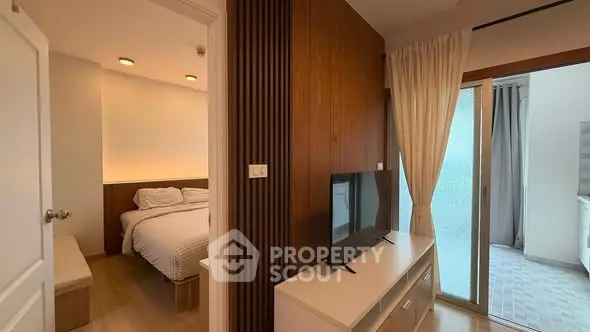 Modern apartment interior with cozy bedroom and stylish living area featuring a TV and sliding glass doors.