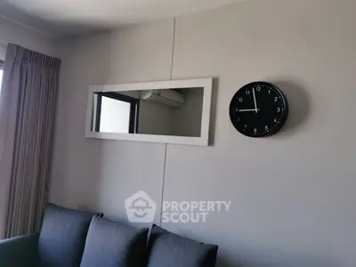 Modern living room with sleek gray sofa, wall mirror, and stylish clock.
