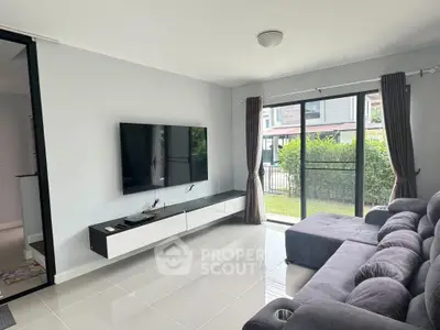 Modern living room with sleek TV setup and large windows overlooking garden.