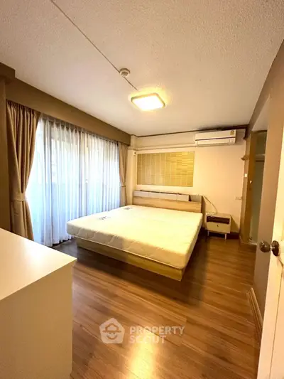 Spacious bedroom with large window and modern furnishings in a cozy apartment.