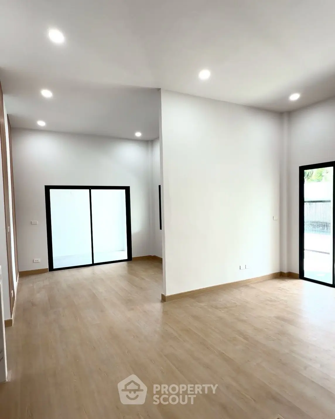 Spacious modern living room with wooden flooring and large windows for natural light.