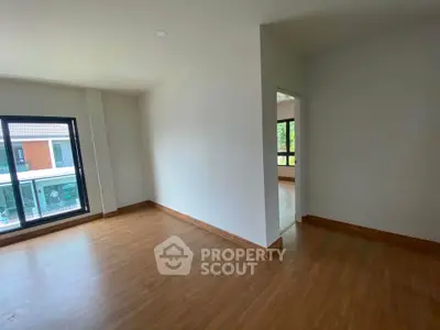 Spacious empty room with wooden flooring and large windows in modern apartment.
