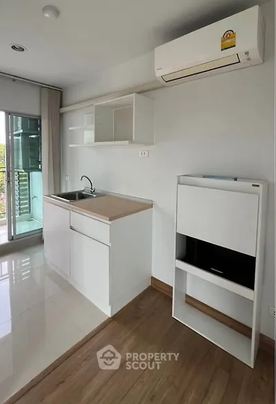 Modern compact kitchen with sleek white cabinets and air conditioning, featuring a bright balcony view.