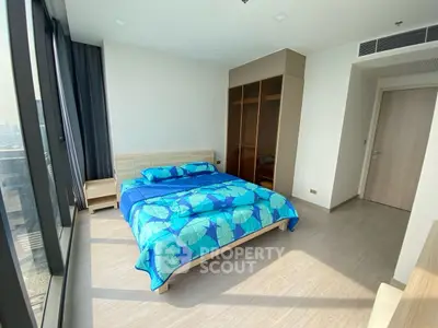 Spacious bedroom with large windows and modern furnishings in a high-rise apartment.