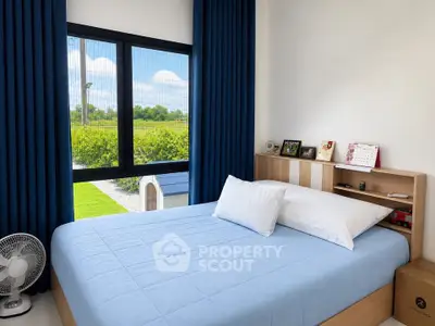 Cozy bedroom with large window and garden view, featuring modern decor and blue accents.