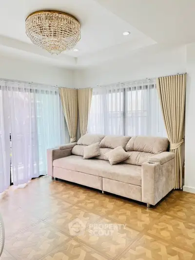 Elegant living room with plush sofa, large windows, and a stunning chandelier, perfect for relaxation and entertaining.