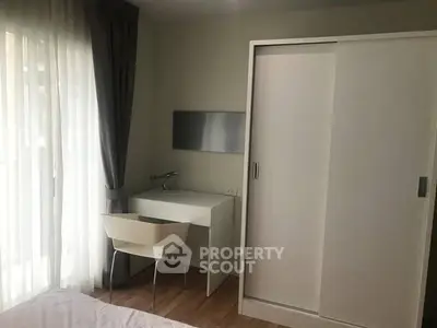 Modern bedroom with sleek white furniture and natural light from large window.