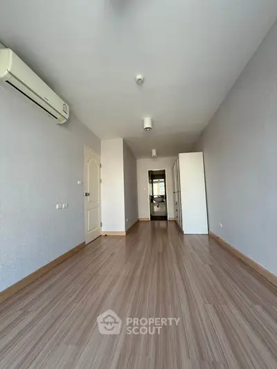 Spacious empty room with wooden flooring and air conditioning, perfect for customization.