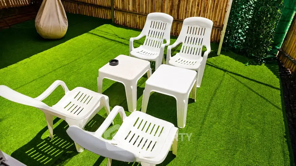 Charming outdoor seating area with white chairs on lush green artificial grass, perfect for relaxation.