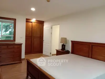 Spacious bedroom with wooden furniture and large window offering natural light.