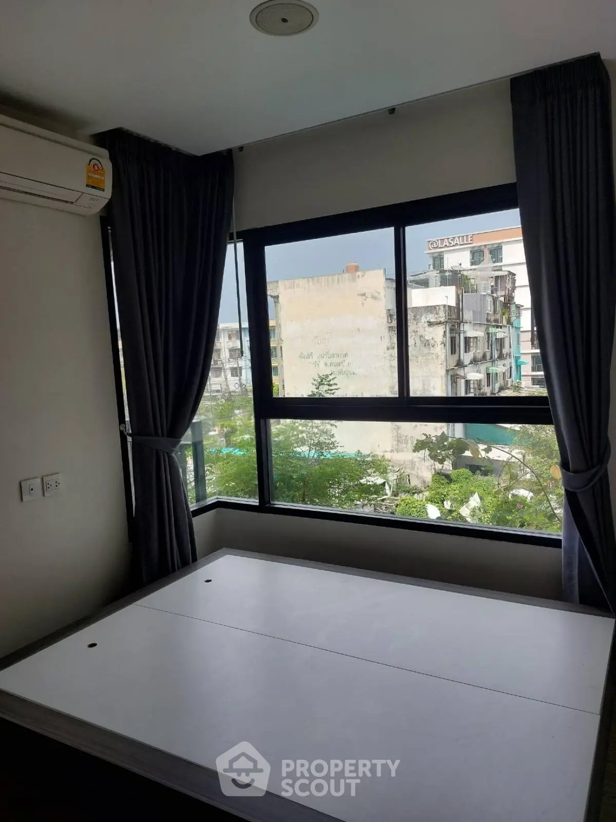 Modern bedroom with large window offering city view, featuring air conditioning and dark curtains.