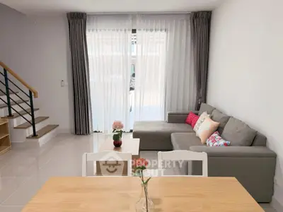 Modern living room with cozy sofa and elegant decor, featuring large windows and stylish staircase.