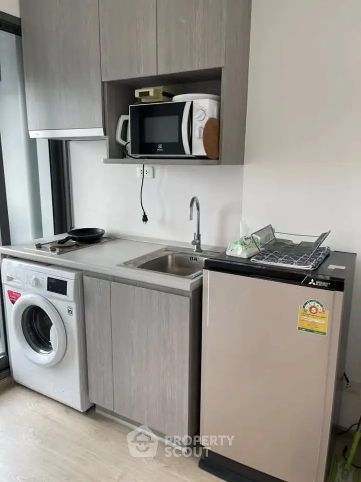 Modern compact kitchen with washing machine and microwave in sleek apartment.