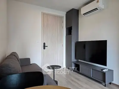 Modern living room with sleek furniture and wall-mounted TV, featuring minimalist design and air conditioning.