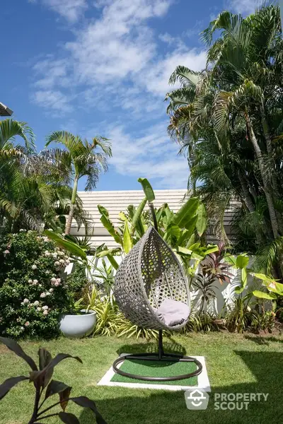 Lush garden with modern hanging chair and tropical plants under blue sky