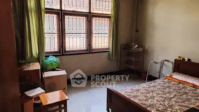 Cozy bedroom with large window and natural light, featuring simple furnishings and tiled floor.