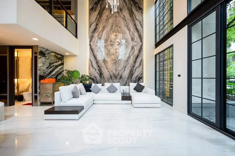 Luxurious modern living room with high ceilings, elegant marble wall, and large windows offering natural light.