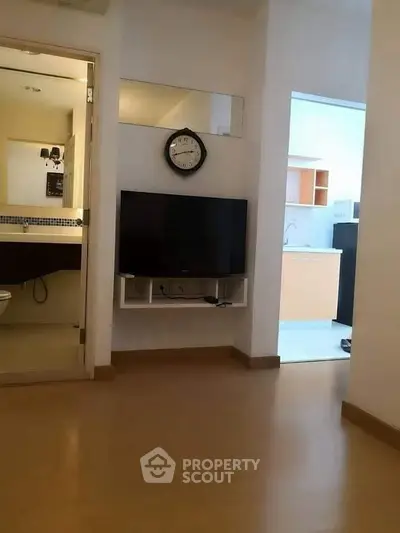 Modern apartment interior with wall-mounted TV and clock, adjacent to bathroom and kitchen.